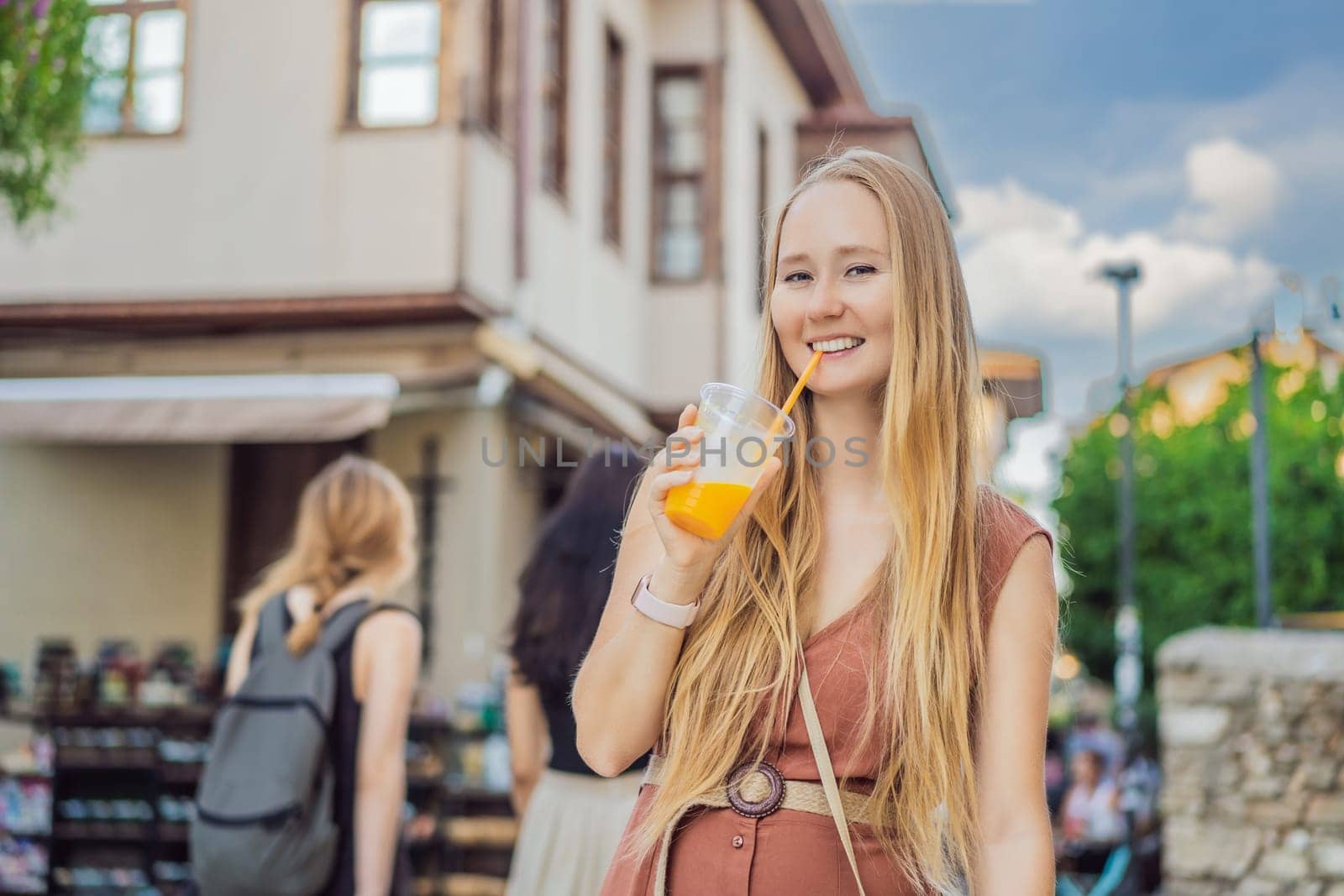 Happy woman tourist with fresh juice on background of old street of Antalya. female tourist traveler discover interesting places and popular attractions and walks in the old city Kalechi of Antalya, Turkey. Turkiye.