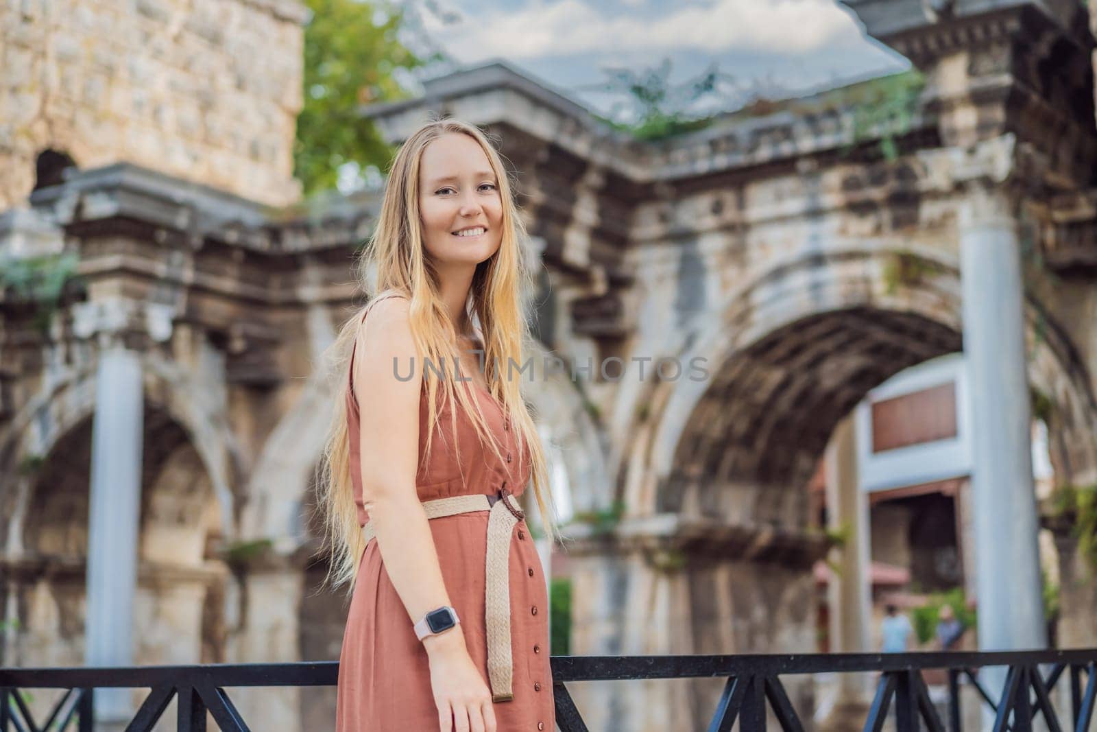Happy female tourist traveler discover interesting places and popular attractions and walks in the old city of Antalya. Hadrian Kapisi turkey landmark city history. Popular tourist attraction - ancient Roman Hadrian Gate in old town Antalya, Turkey on a summer day. Turkiye.