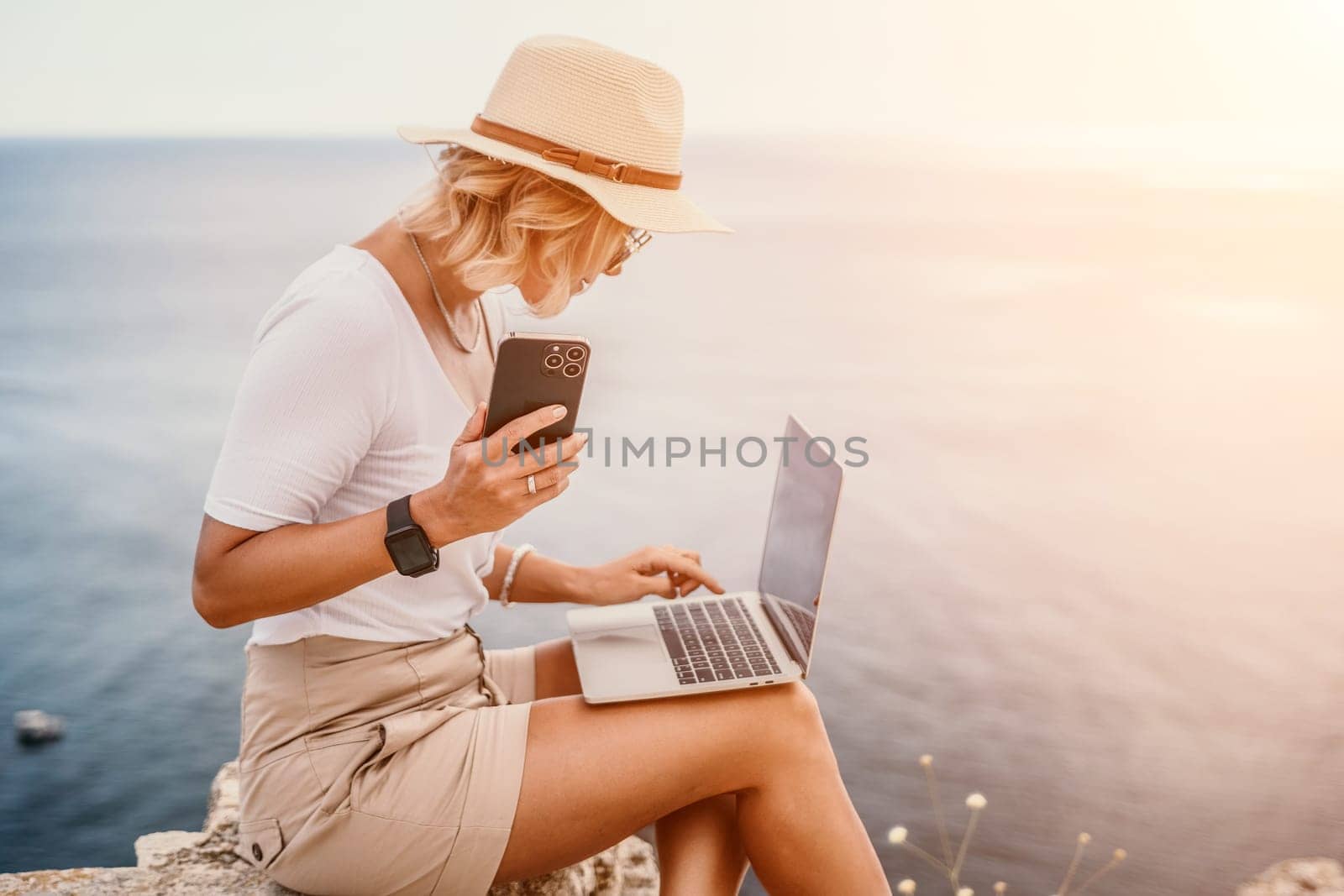 Digital nomad, Business woman working on laptop by the sea. Pretty lady typing on computer by the sea at sunset, makes a business transaction online from a distance. Freelance, remote work on vacation by panophotograph