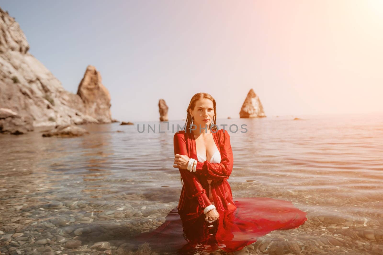 Woman travel sea. Happy tourist in red dress enjoy taking picture outdoors for memories. Woman traveler posing in sea beach, surrounded by volcanic mountains, sharing travel adventure journey by panophotograph