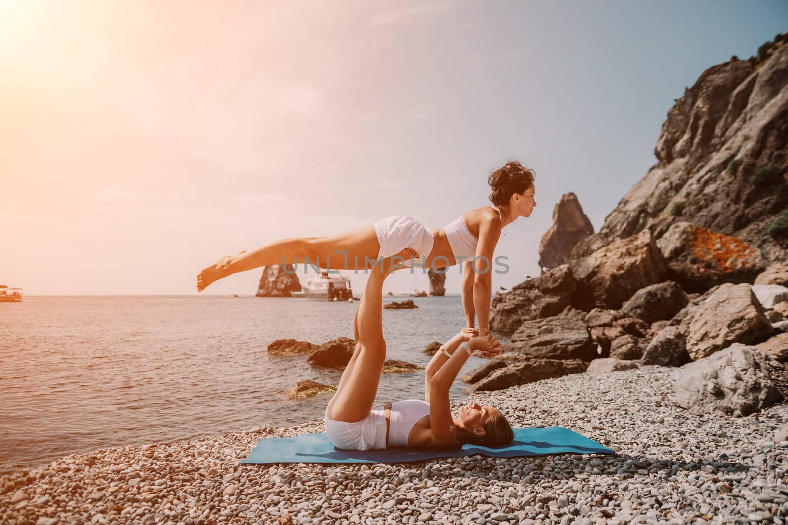 Woman sea yoga. Two happy women practicing yoga on the beach with ocean and rock mountains. Motivation and inspirational fit and exercising. Healthy lifestyle outdoors in nature, fitness concept. by panophotograph