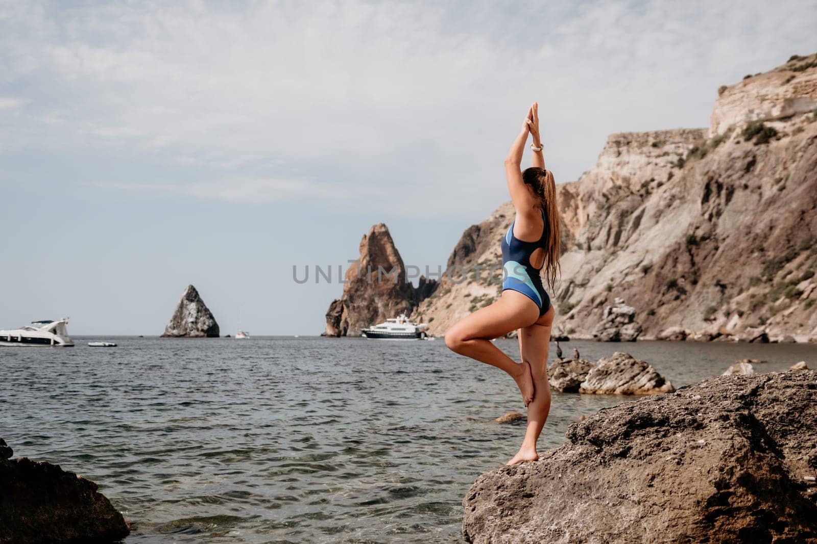 Woman sea yoga. Back view of free calm happy satisfied woman with long hair standing on top rock with yoga position against of sky by the sea. Healthy lifestyle outdoors in nature, fitness concept.