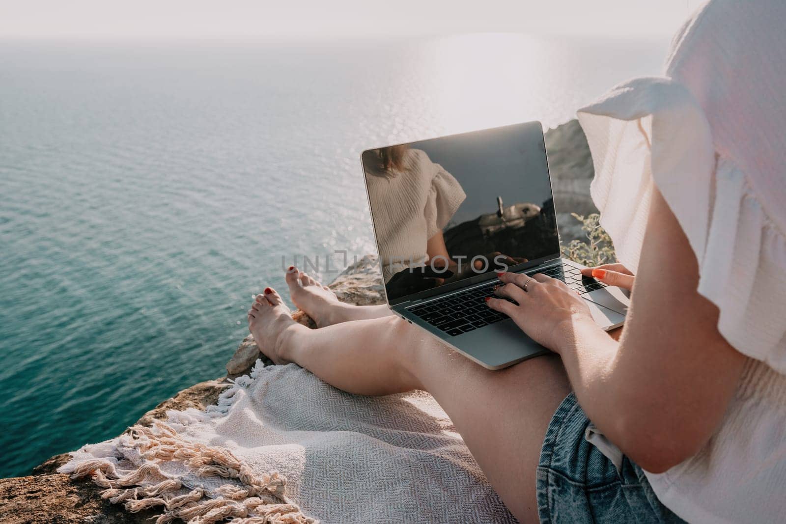 Woman sea laptop. Business woman in yellow hat working on laptop by sea. Close up on hands of pretty lady typing on computer outdoors summer day. Freelance, digital nomad, travel and holidays concept.