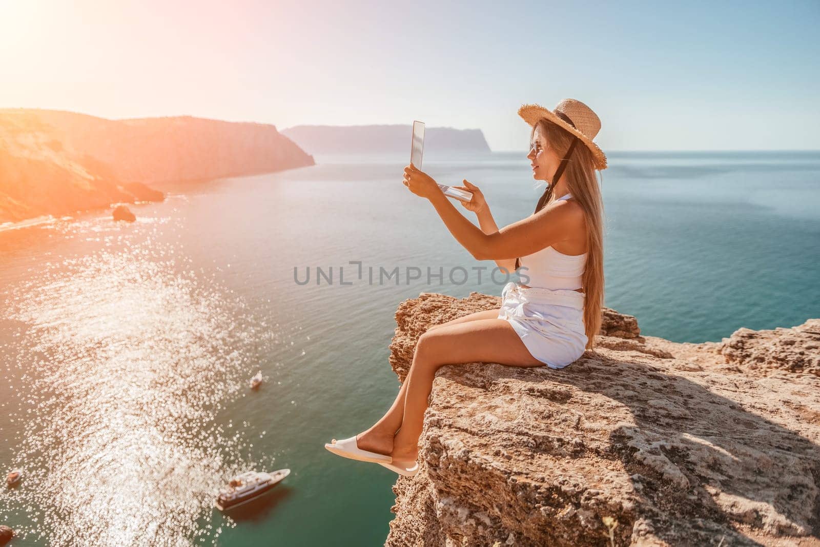 Woman laptop sea. Working remotely on seashore. Happy successful woman female freelancer in straw hat working on laptop by the sea at sunset. Freelance, remote work on vacation by panophotograph