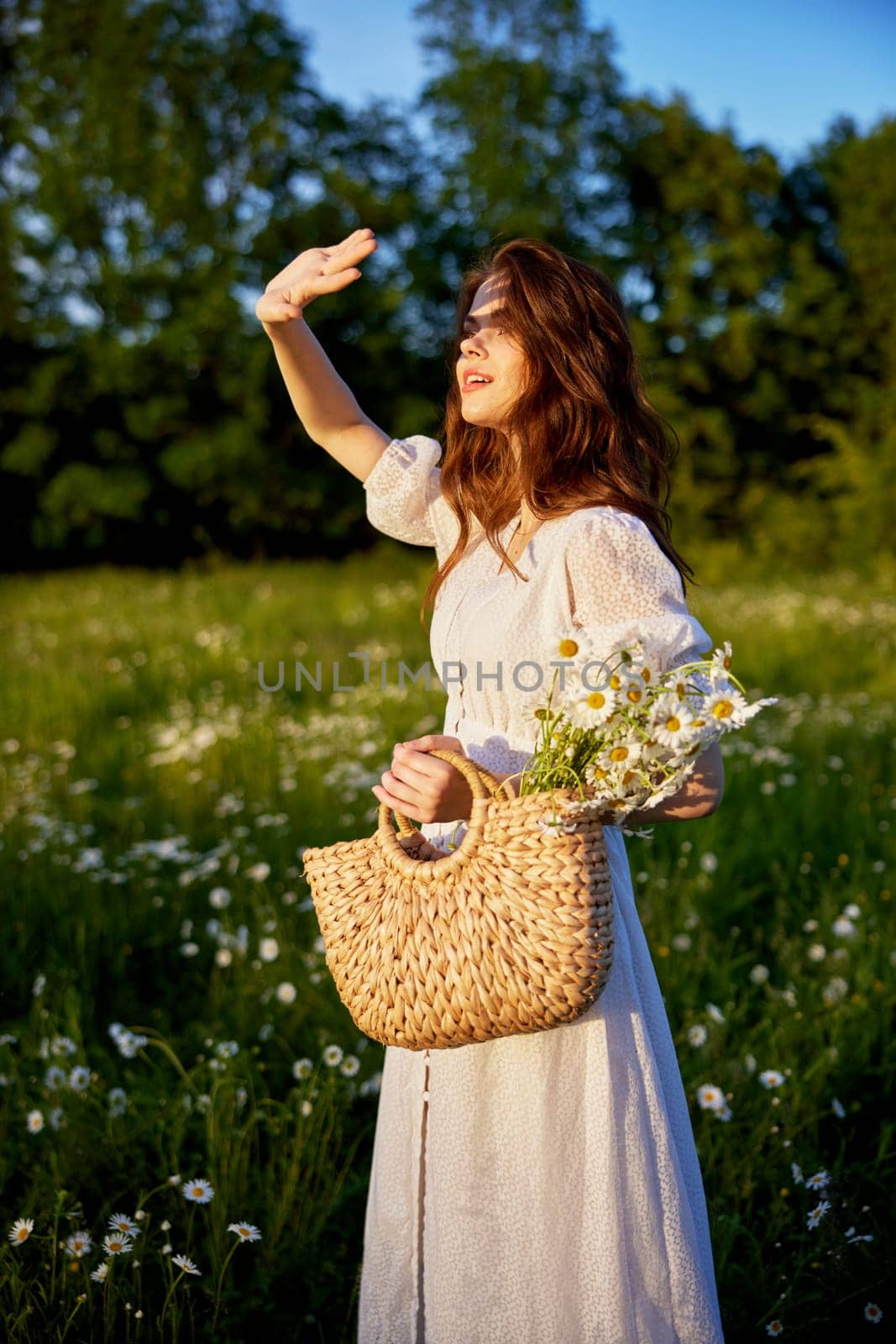 a woman in a white dress stands in nature covering herself with her hands from the bright sun by Vichizh