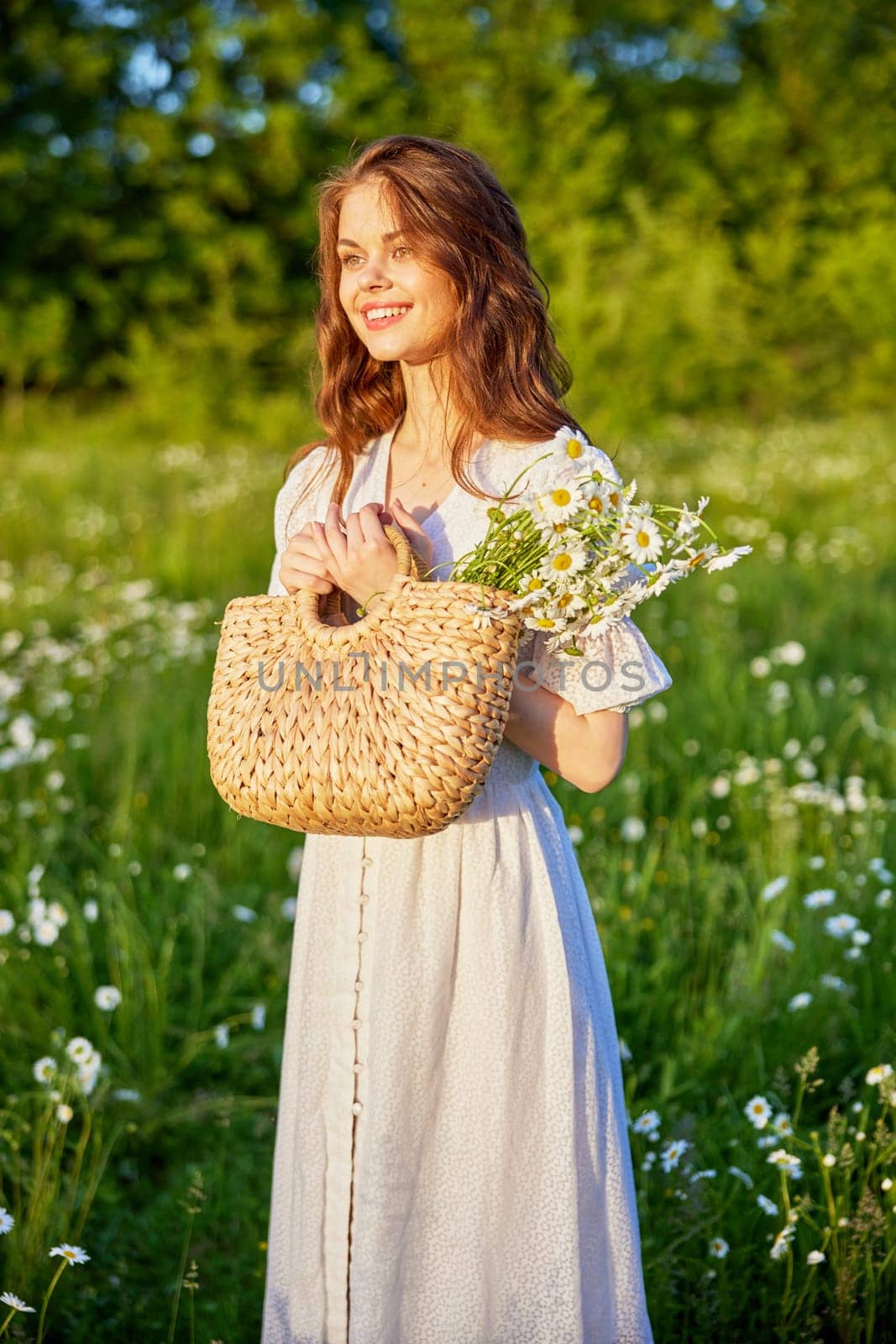 beautiful woman laughing in nature in a chamomile field holding a wicker basket in her hands by Vichizh