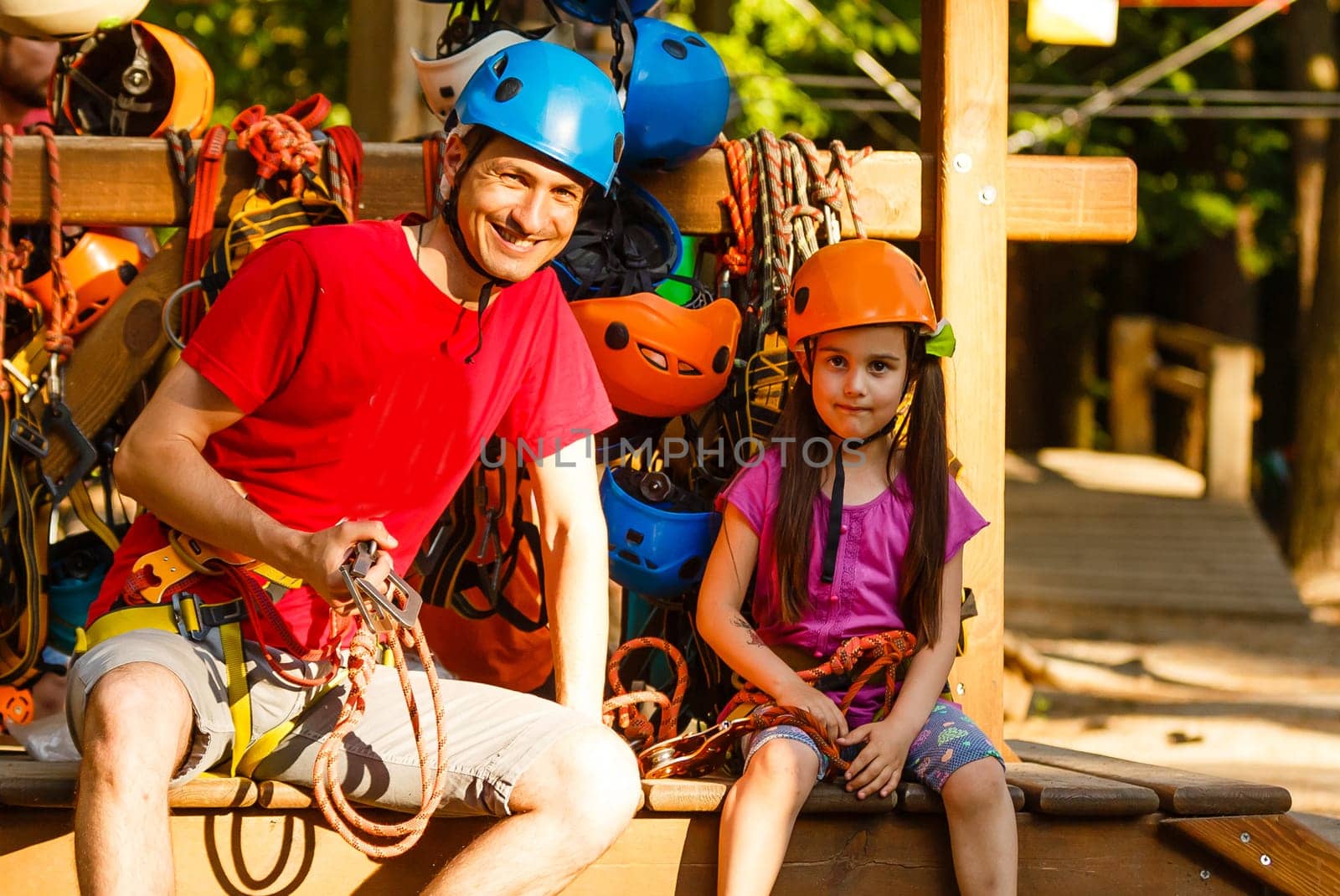 Adorable little girl enjoying her time in a rope playground structure at adventure park, her father supporting her, family weekend activities