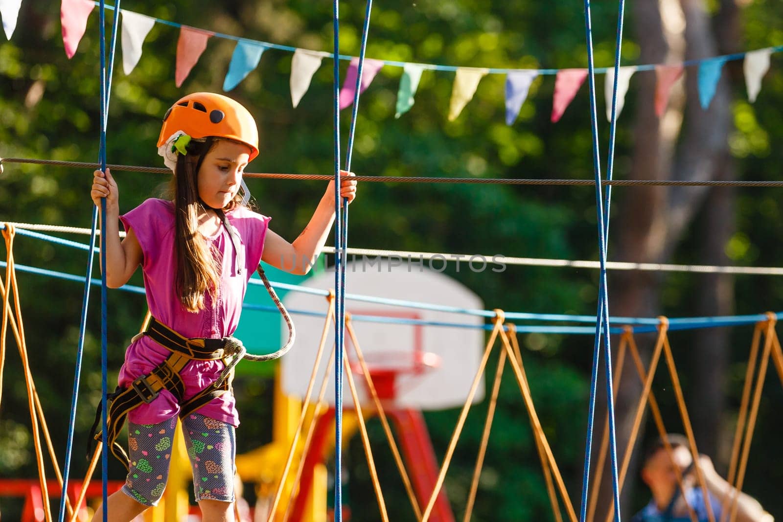 Happy school girl enjoying activity in a climbing adventure park on a summer day.