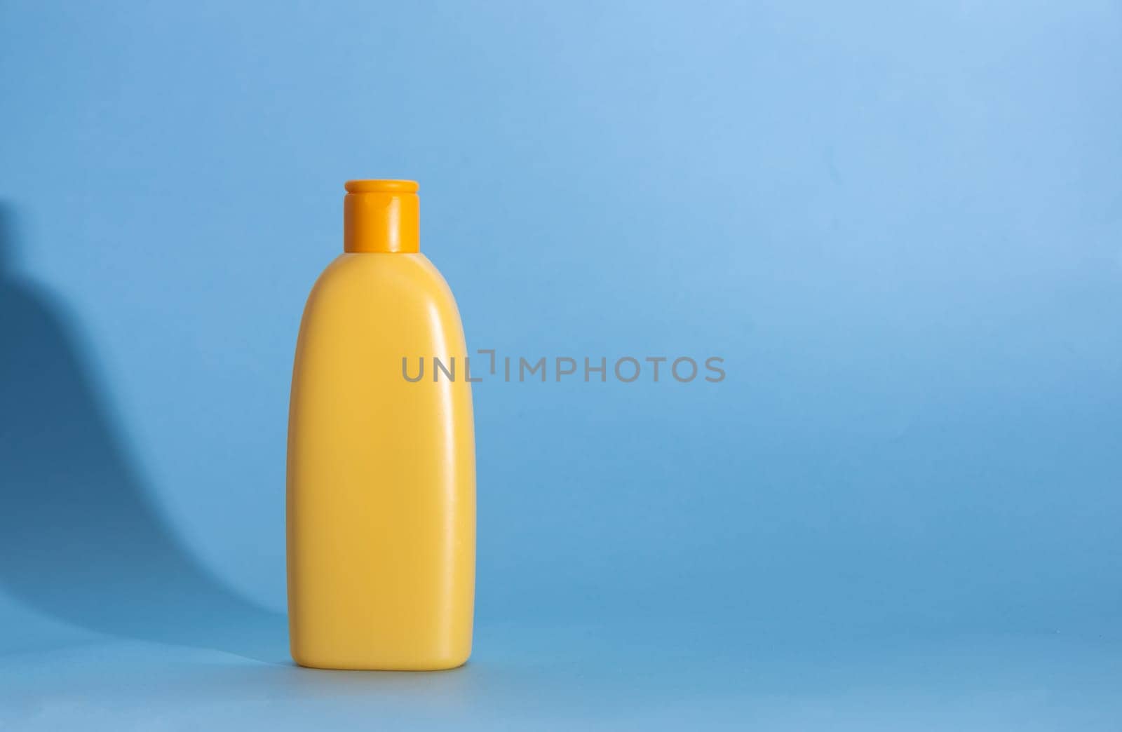 Yellow plastic cosmetic bottle on blue background. Kids hair shampoo, body lotion or sunscreen cream. Mock up, template. by Ri6ka
