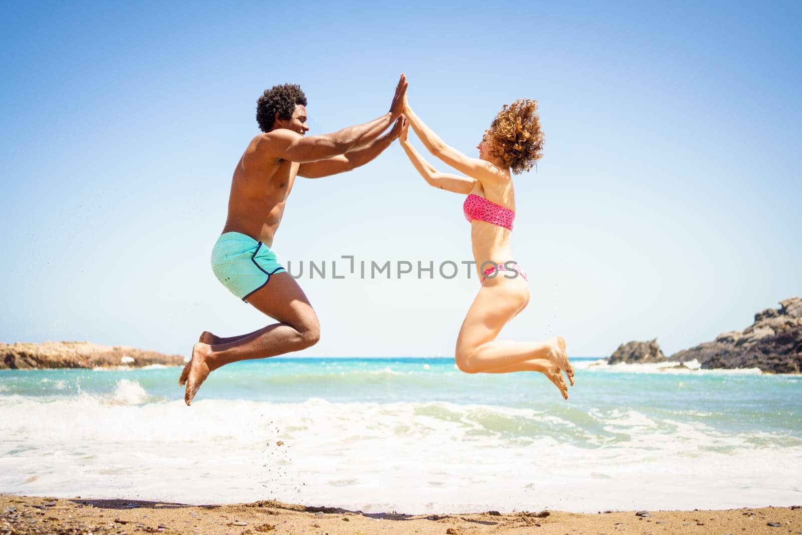Happy multiethnic couple jumping near sea by javiindy