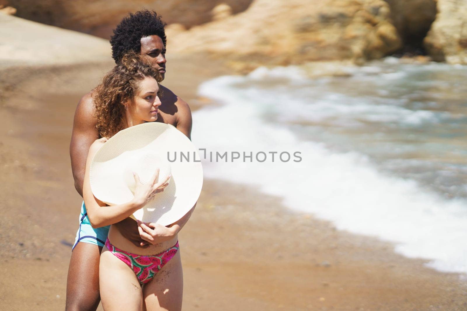 Multiracial couple hugging on beach by javiindy
