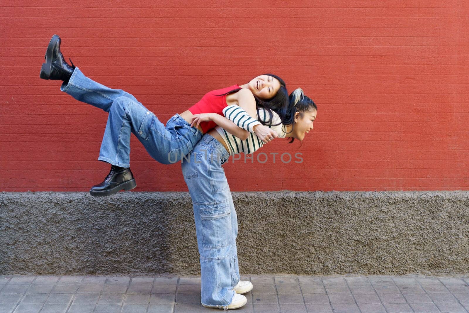 Happy Asian female lifting friend on back by javiindy