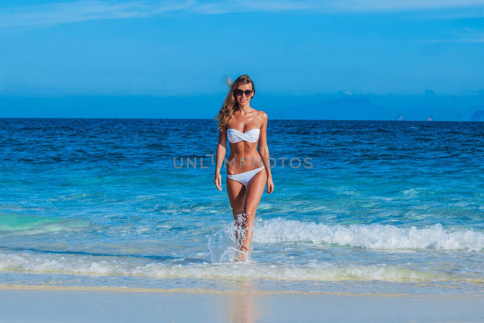 Pretty smiling girl in bikini walking at tropical sea beach