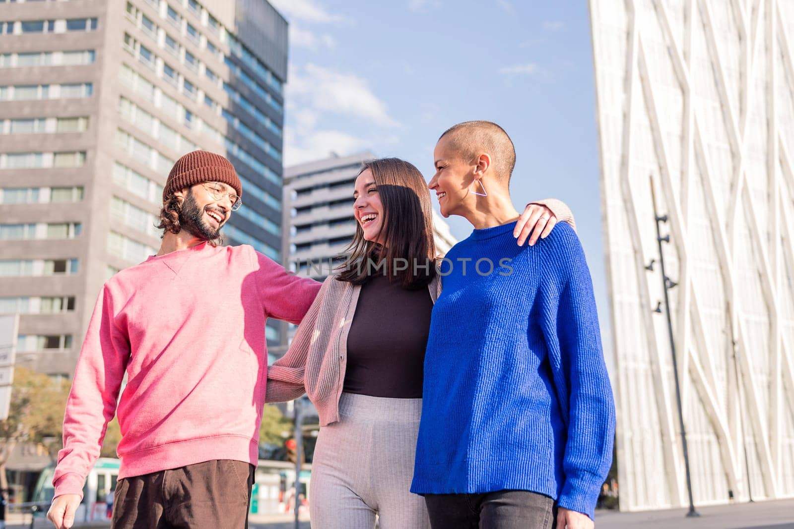 three young friends, one man and two women, laughing and hugging during a casual walk, concept of friendship and urban lifestyle