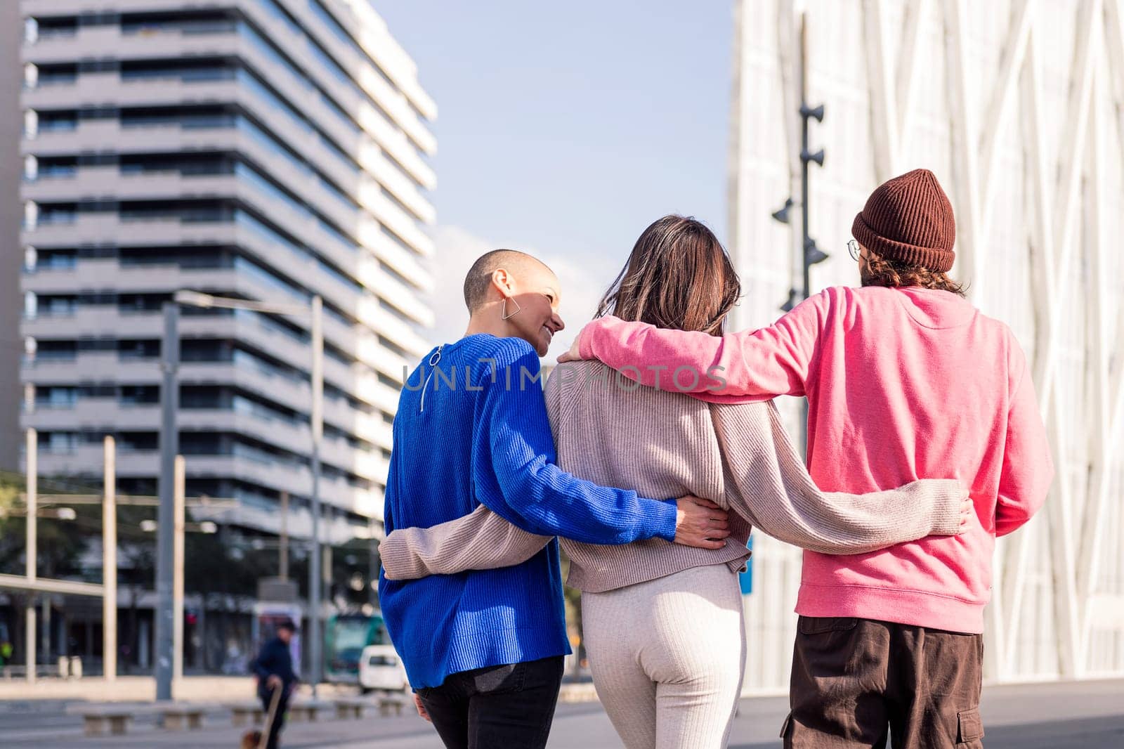 rear view of three friends, one man and two women, taking a peaceful stroll together on a sunny day, concept of friendship and urban lifestyle