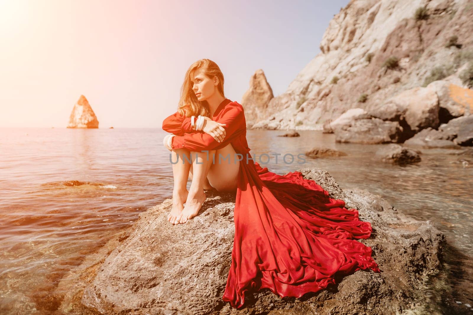 Woman travel sea. Happy tourist in red dress enjoy taking picture outdoors for memories. Woman traveler posing on the rock at sea bay surrounded by volcanic mountains, sharing travel adventure journey by panophotograph