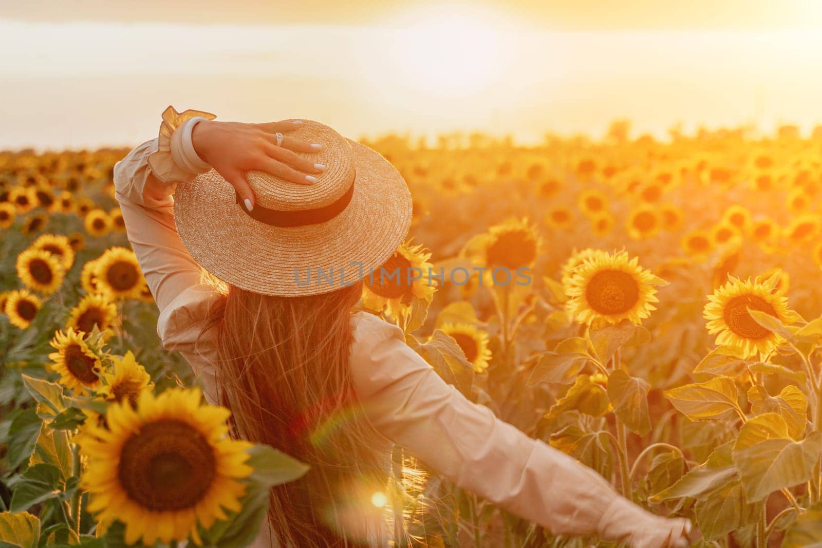 Woman in Sunflower Field: Happy girl in a straw hat posing in a vast field of sunflowers at sunset, enjoy taking picture outdoors for memories. Summer time. by panophotograph