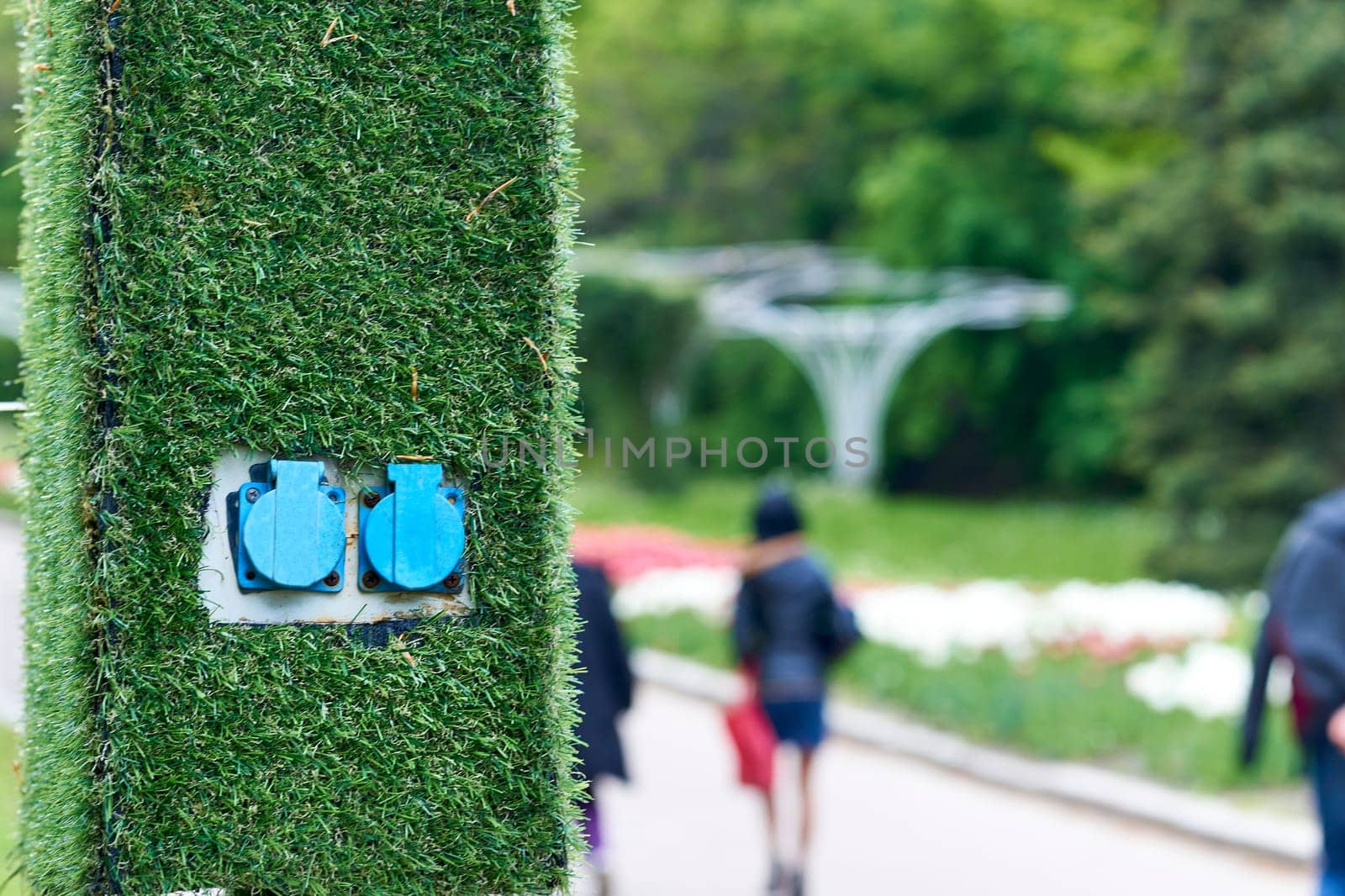 an electrical device receiving a plug or light bulb to make a connection. Electric sockets for charging on a pole with artificial green grass in the park