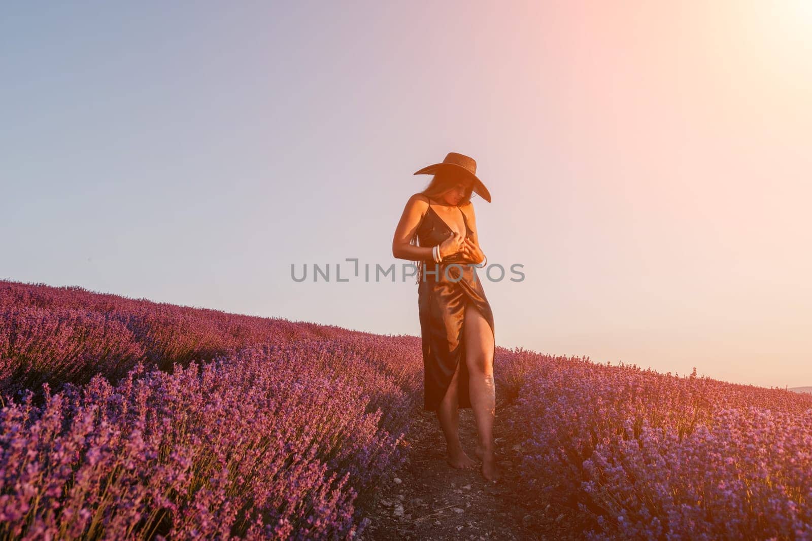 Woman lavender field. Happy carefree woman in black dress and hat with large brim walking in a lavender field during sunset. Perfect for inspirational and warm concepts in travel and wanderlust. by panophotograph