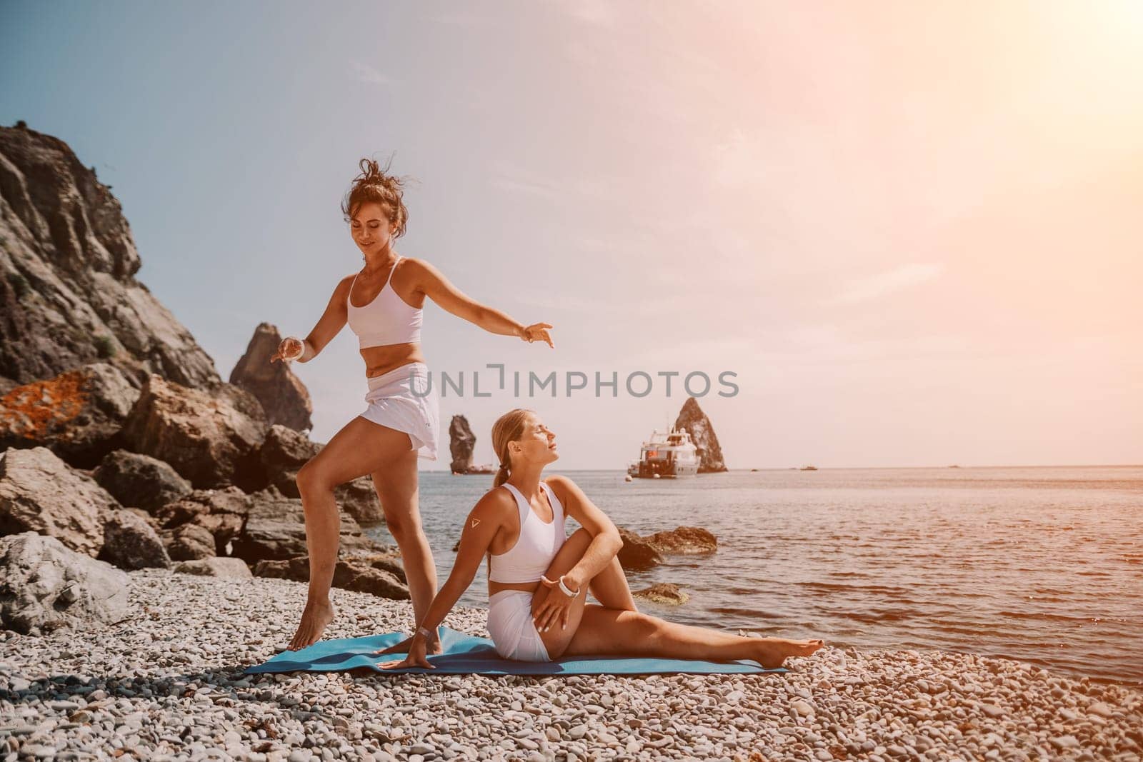 Woman sea yoga. Two happy women practicing yoga on the beach with ocean and rock mountains. Motivation and inspirational fit and exercising. Healthy lifestyle outdoors in nature, fitness concept. by panophotograph