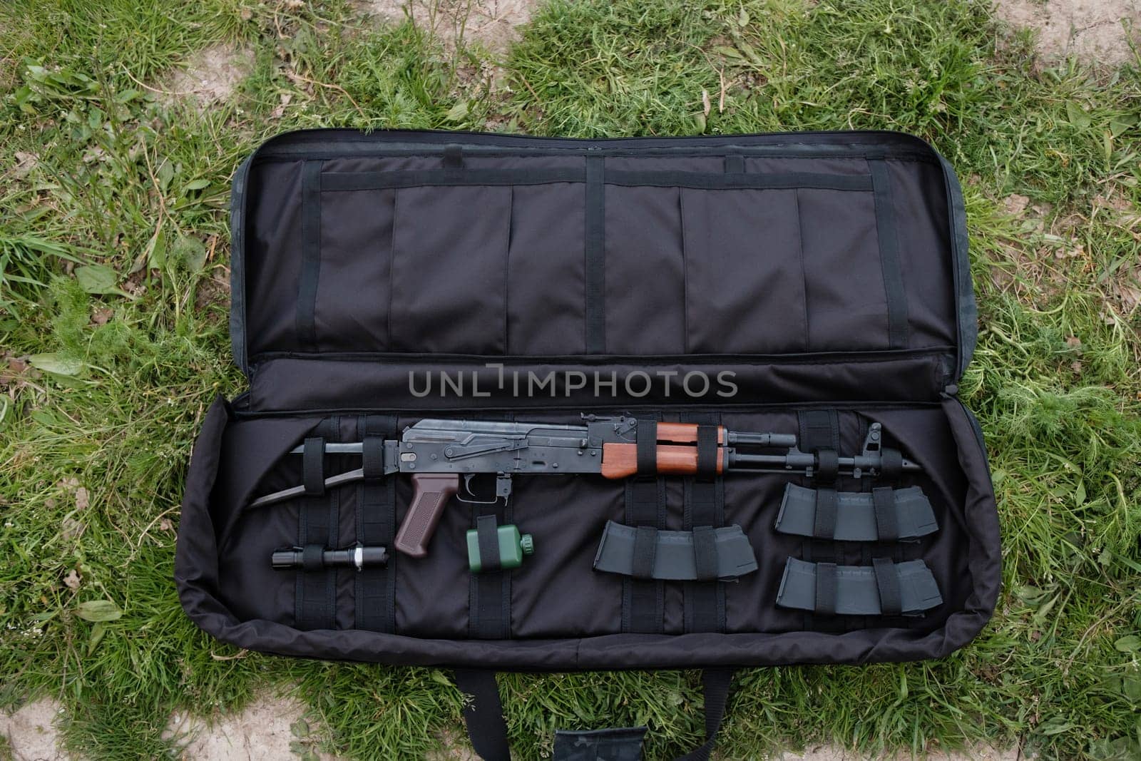 Uncovered gun case with AK-47, magazines, and flashlight lying on the ground by Symonenko