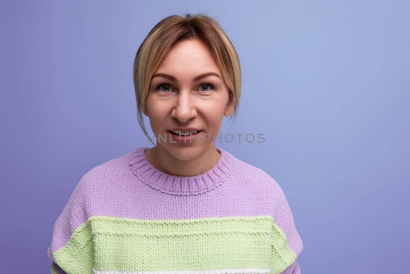 bright joyful energetic blond woman in a casual striped sweater on a purple background by TRMK