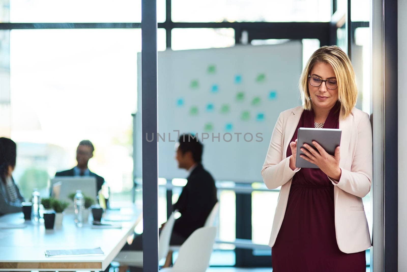 Getting her notes before heading into the meeting. a beautiful young businesswoman using a tablet in the workplace. by YuriArcurs