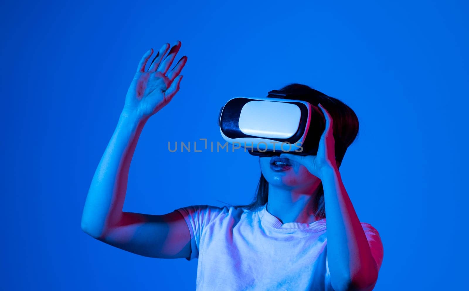 Close up of young woman stands in studio wearing VR glasses and swiping scrolling zooming with hands in a virtual space while interacting with a objects in a metaverse. Virtual reality technology. by vovsht