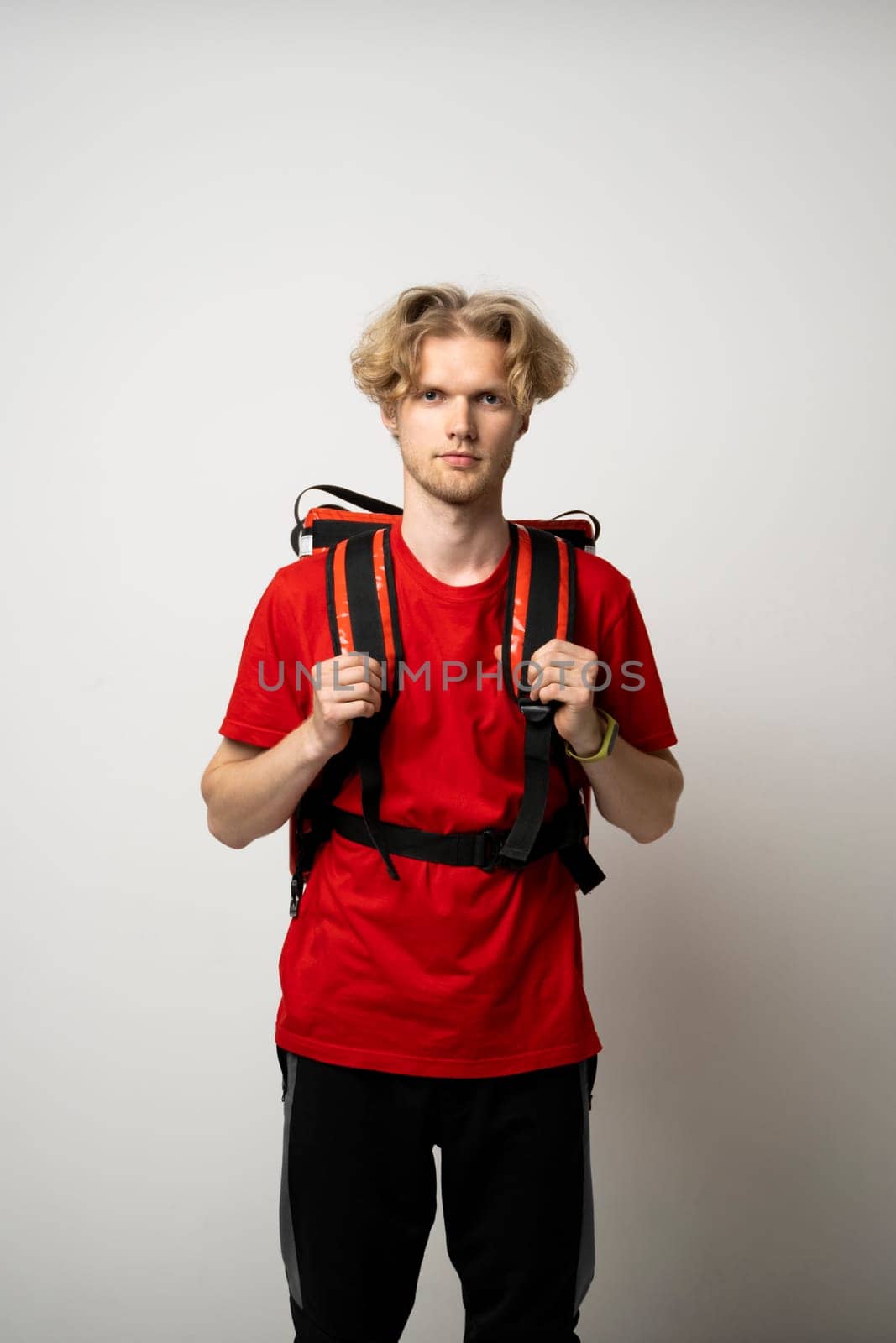 Delivery Service Cocnept. Portrait of male courier wearing red uniform and thermo backpack bag looking at camera isolated on white studio background