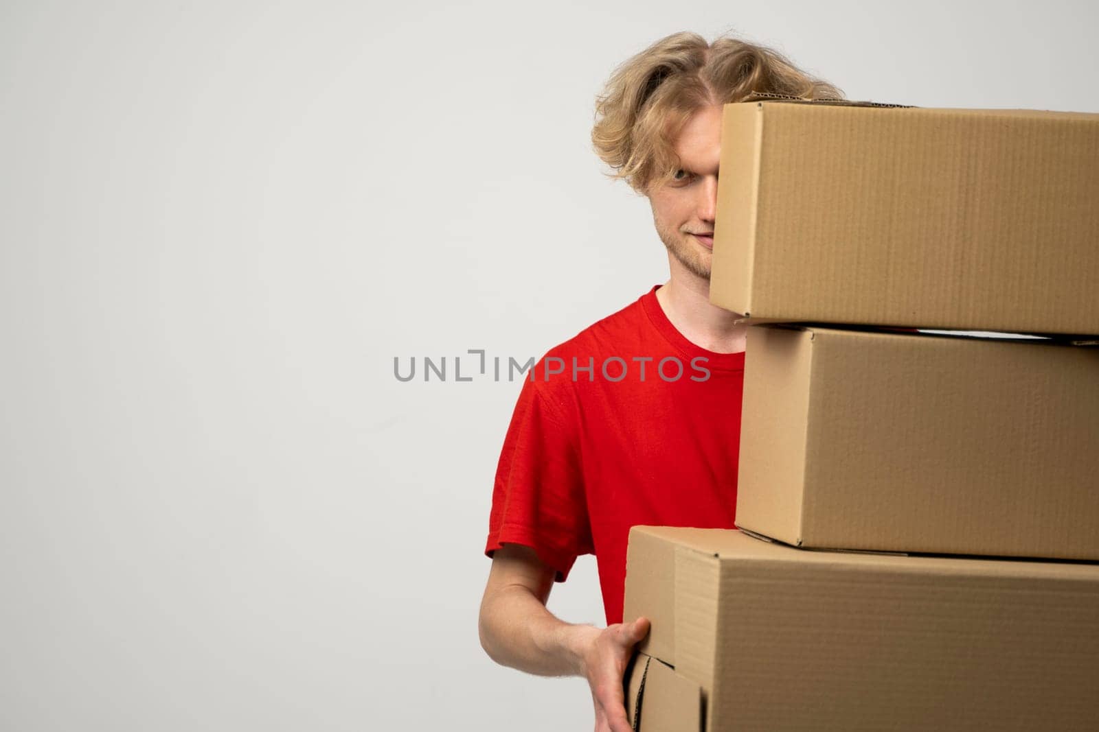 Courier in a red uniform holding a stack of cardboard boxes. Delivery man delivering postal packages over white studio background