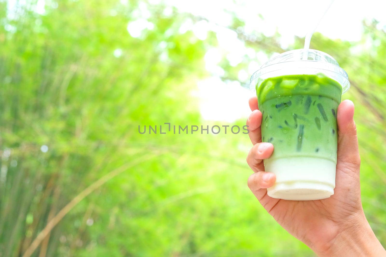 Woman hand holding the glass iced matcha latte green tea coffee on spring nature background