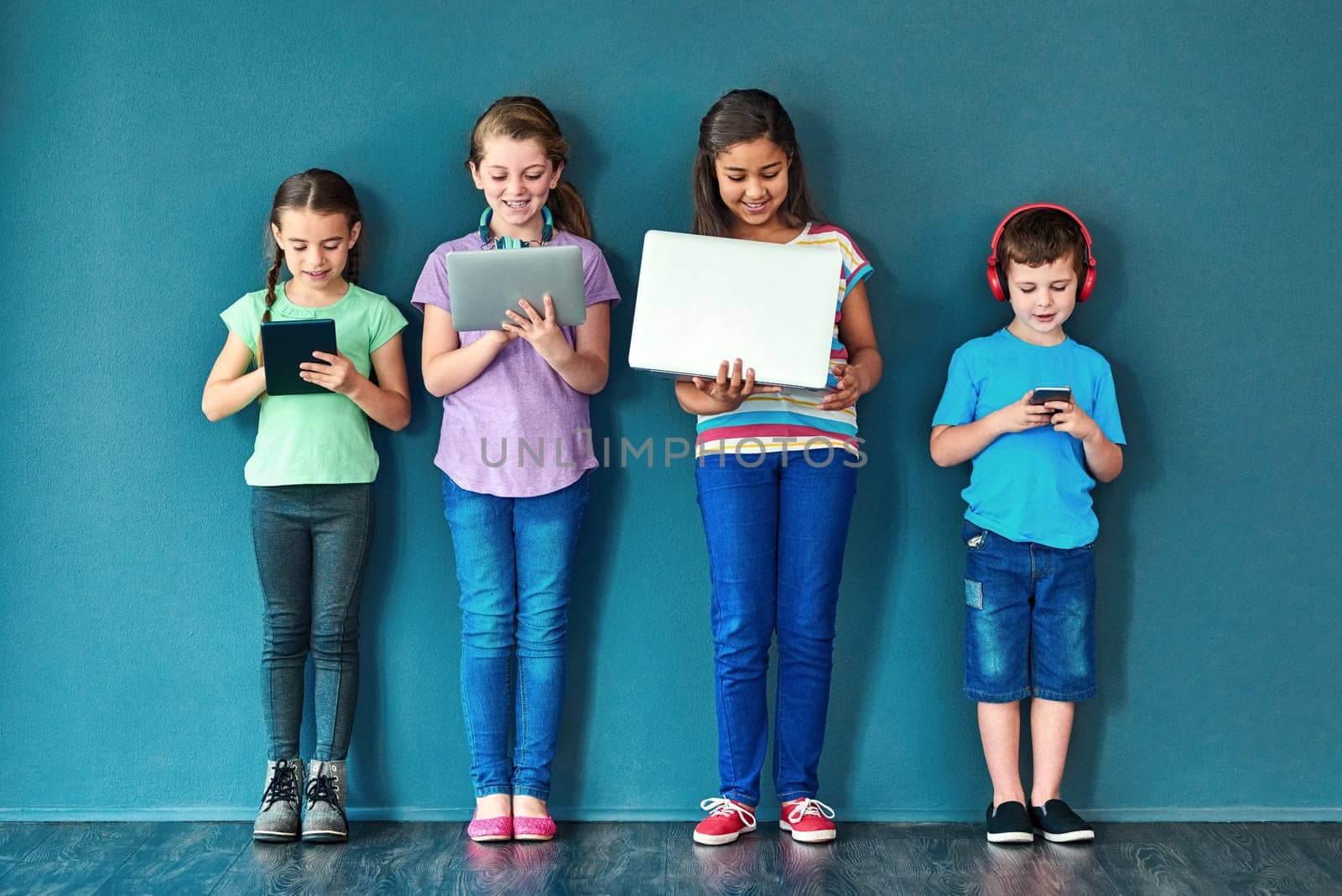 Leaving wireless technology in the hands of kids. Studio shot of a group of kids using wireless technology against a blue background. by YuriArcurs