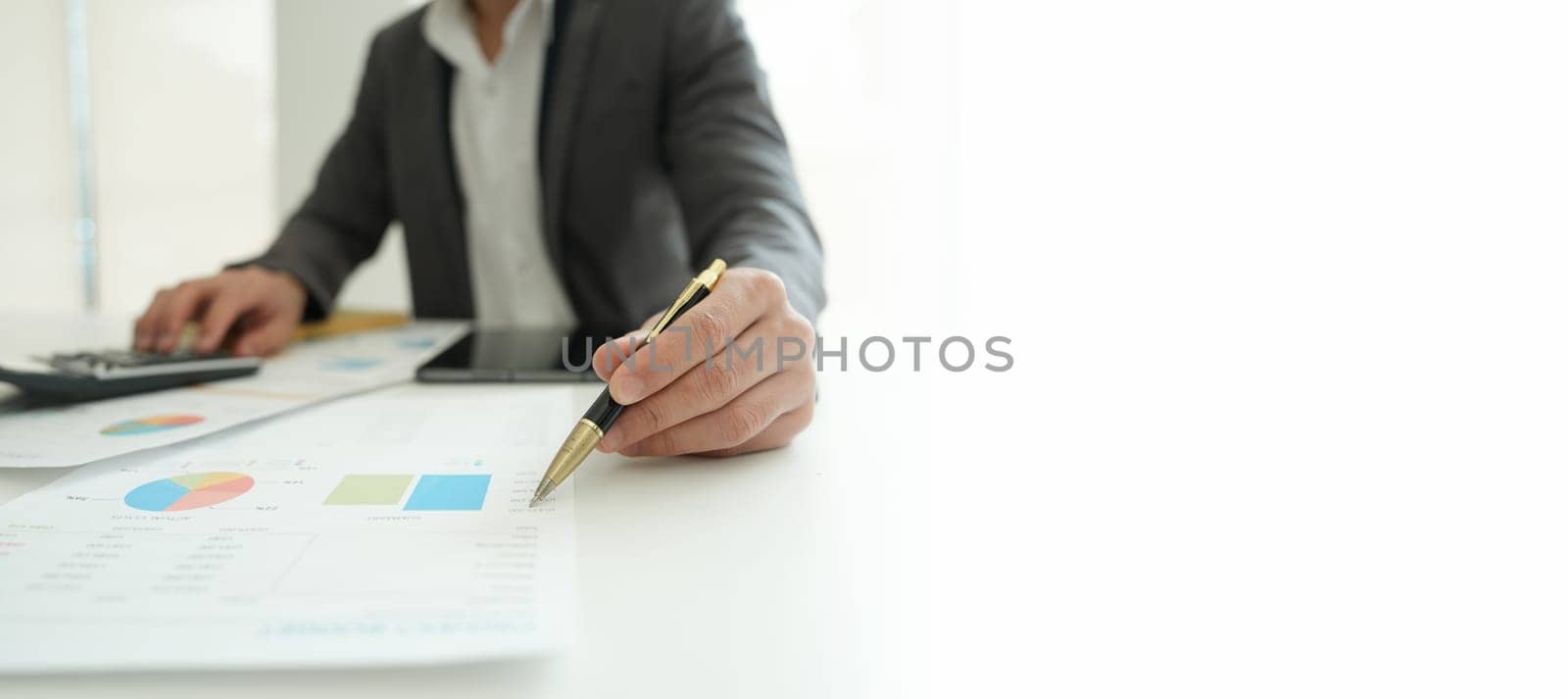 businessman or accountant working on calculator and laptop computer to calculate business data during using accountancy document at office. by Manastrong