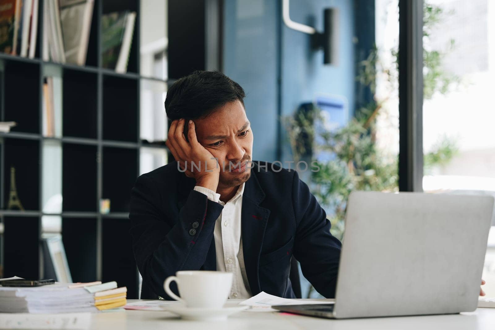 Portrait of business owner, man using computer and financial statements Anxious expression on expanding the market to increase the ability to invest in business. by Manastrong