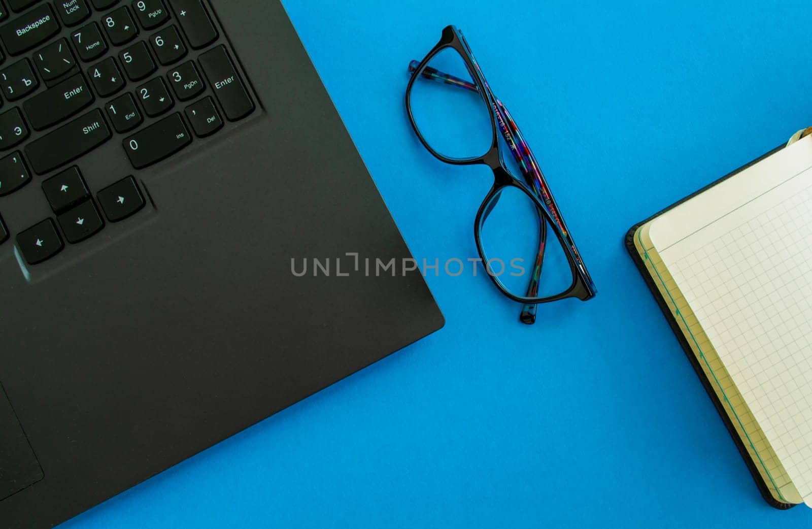 desktop. Laptop, glasses and notepad on a blue background. Mockup diary. Business, freelancing, back to school.