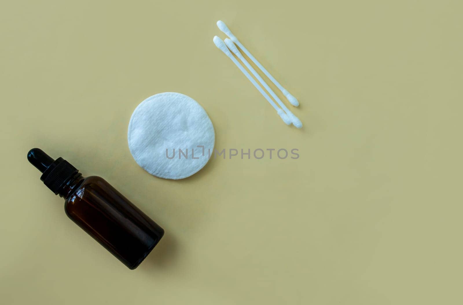 Flat lay bottle with a pipette for cosmetics, cotton buds and a cotton pad on a beige background.  by Yuka777