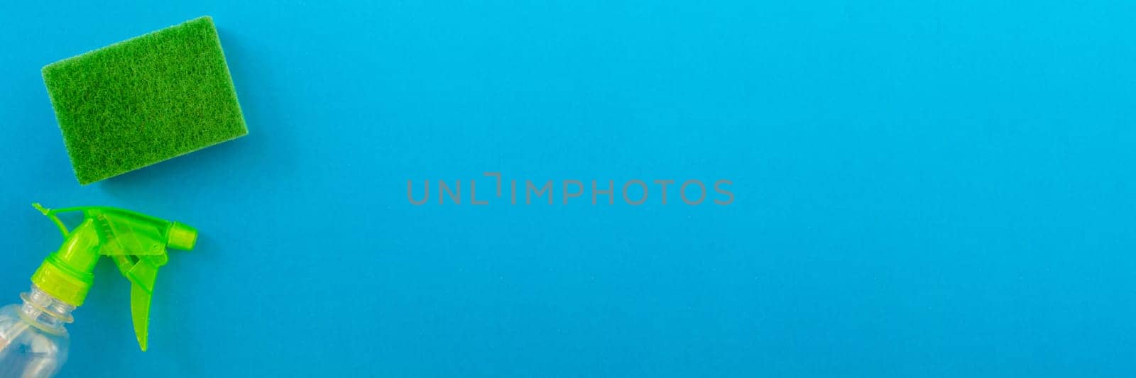 Banner.  Cleaning. Flat lay green sponge and cleaning product on a blue background. Cleaning supplies, top view.