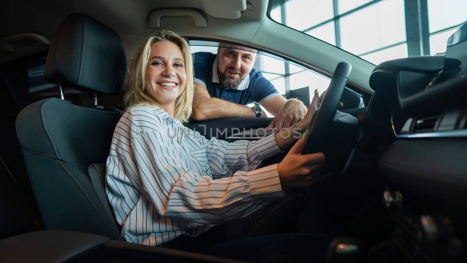 Happy caucasian couple chooses a new car in a car dealership for his wife. A young woman is driving