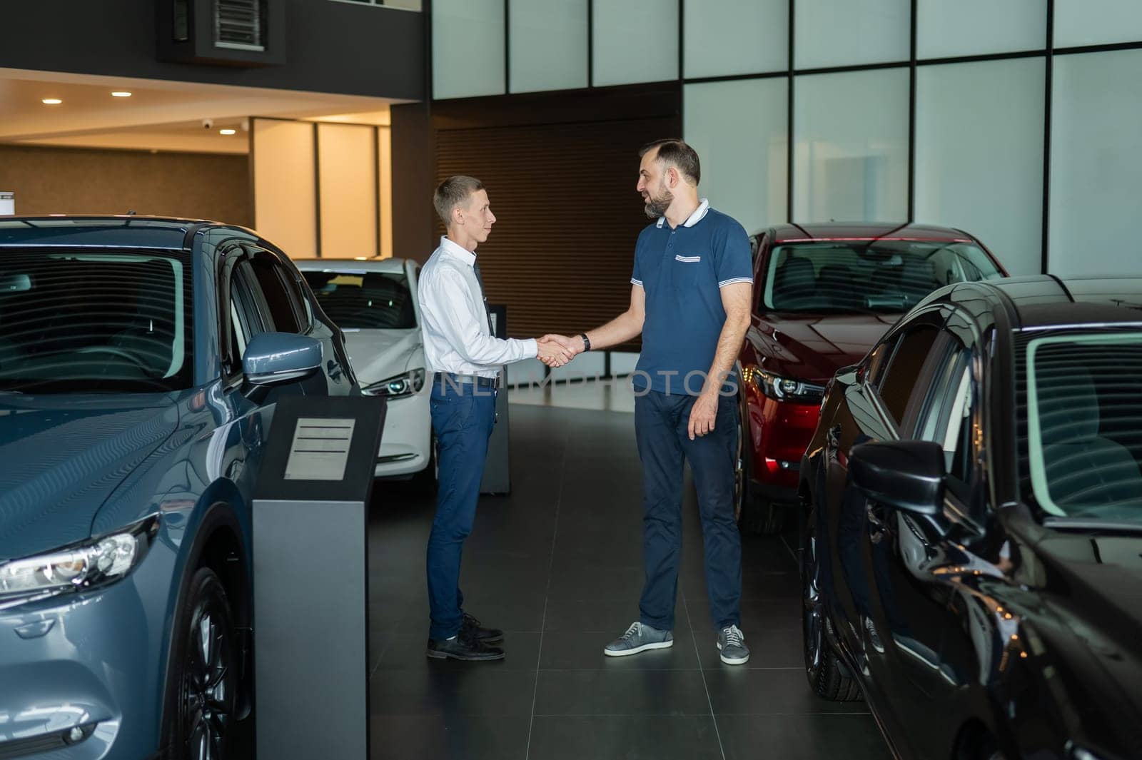 Seller and buyer shake hands in a car dealership. Caucasian man buys a car