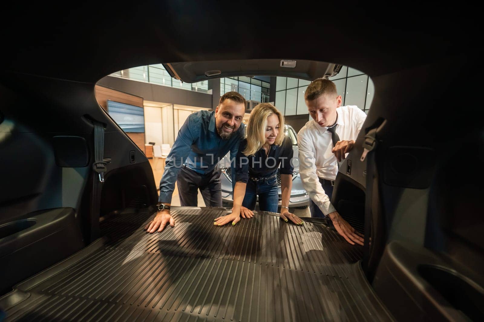 The seller demonstrates the interior of the car to buyers. Caucasian couple chooses a car