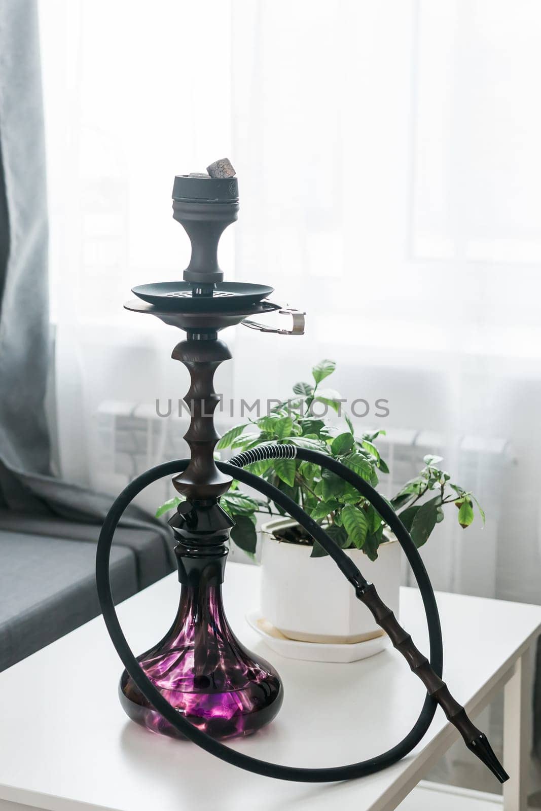 Hookah shisha with glass flask and metal bowl in room background. Traditional Eastern vacation for relaxation by Satura86