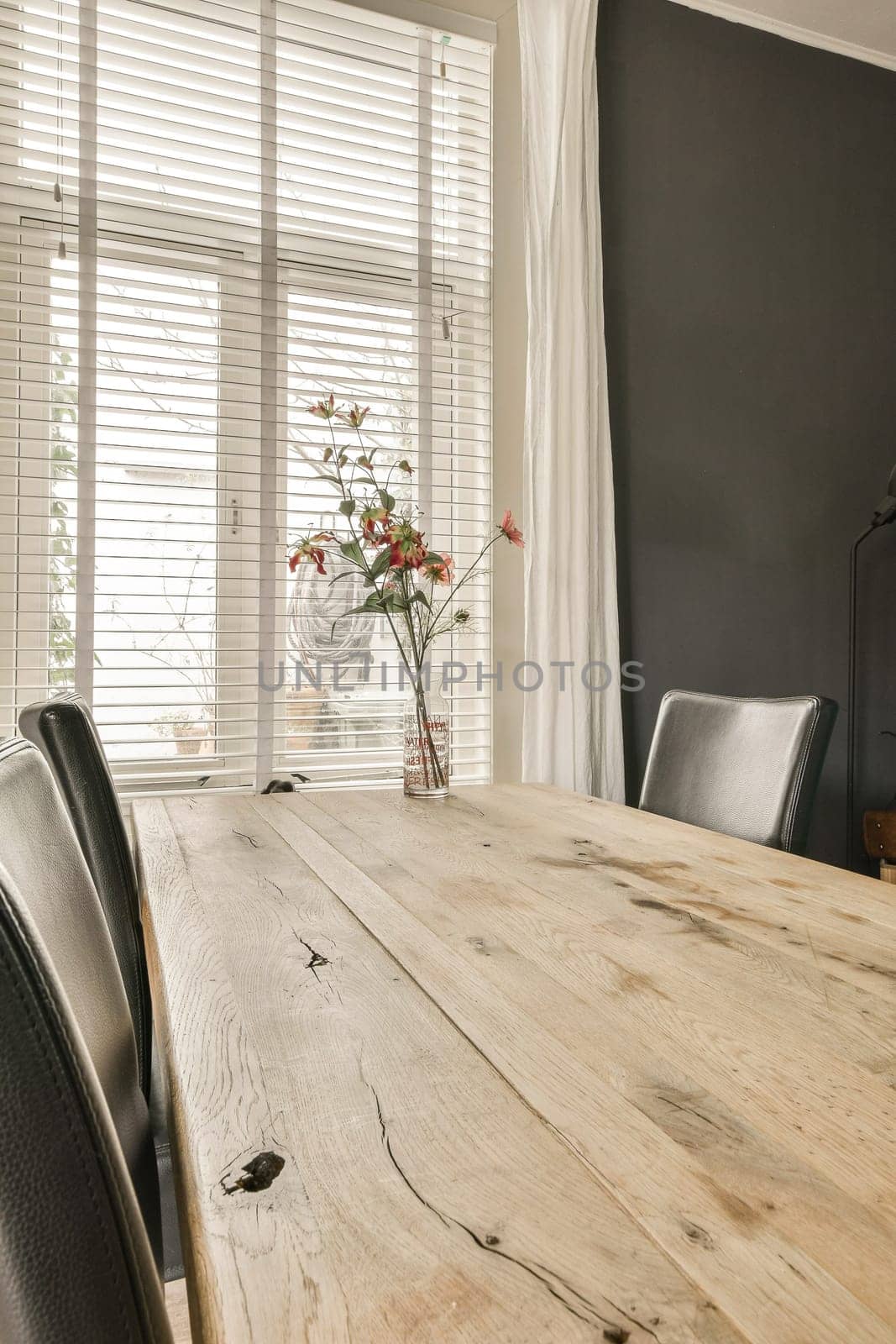 a dining table and chairs in a room with white blinds on the window behind it is a vase of flowers
