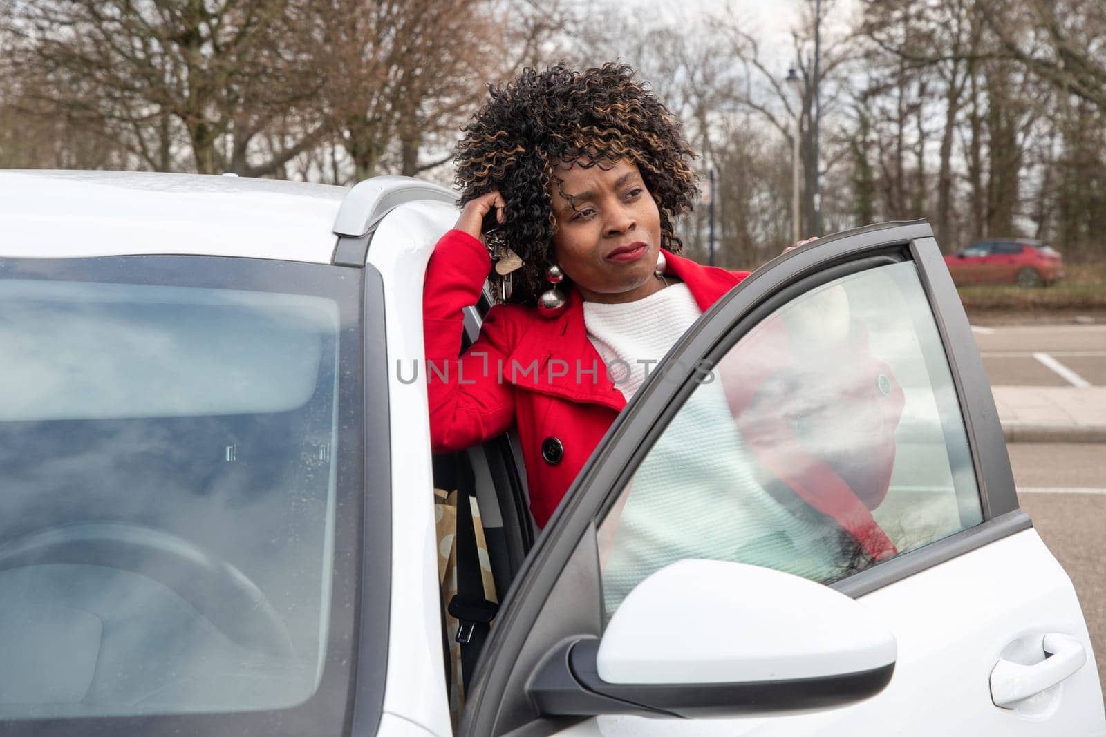 African american beautiful woman in a red coat posing on the street with her car by KaterinaDalemans