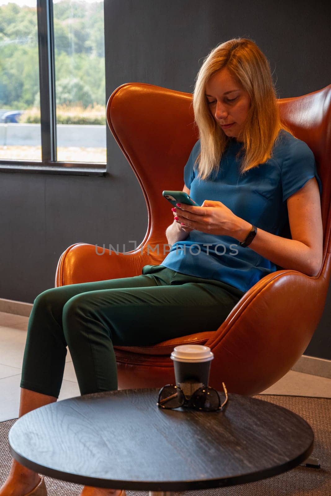 positive blonde businesswoman holding a mobile phone, happy to receive a message from her best friend or colleague, sitting in a cozy cafeteria at the table, High quality photo