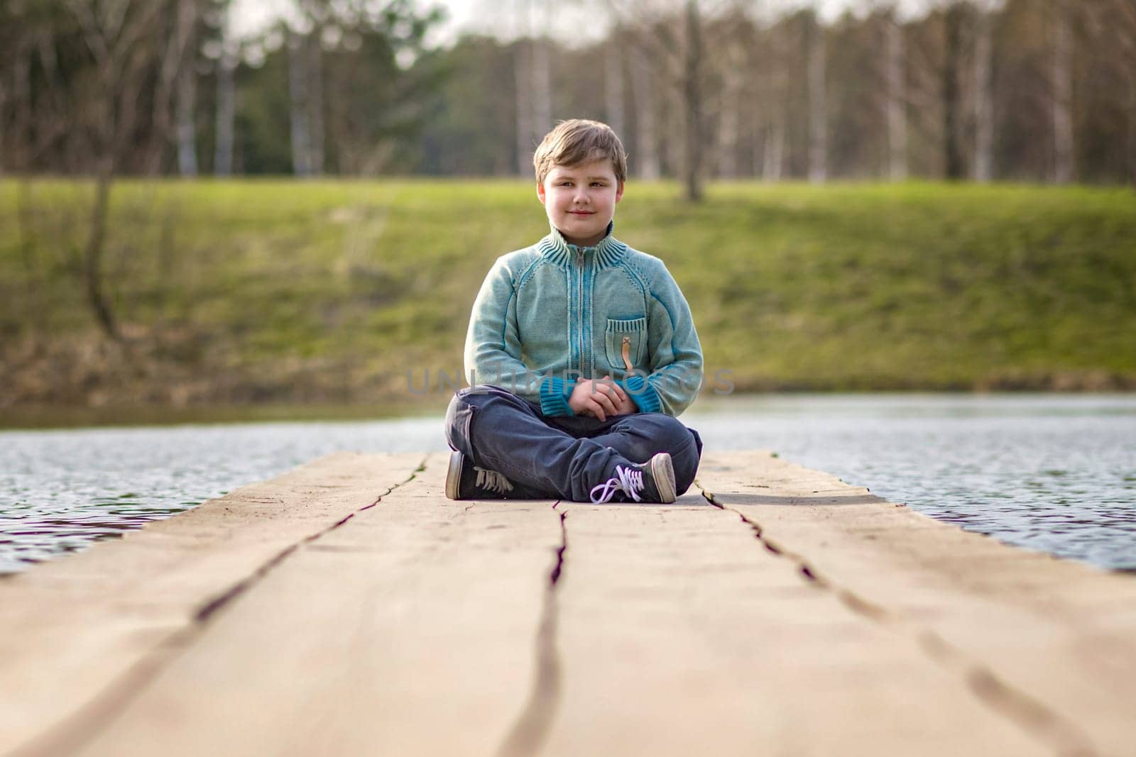 A boy is sitting on a bridge in a green park. The path is a bridge over the lake. by Alina_Lebed