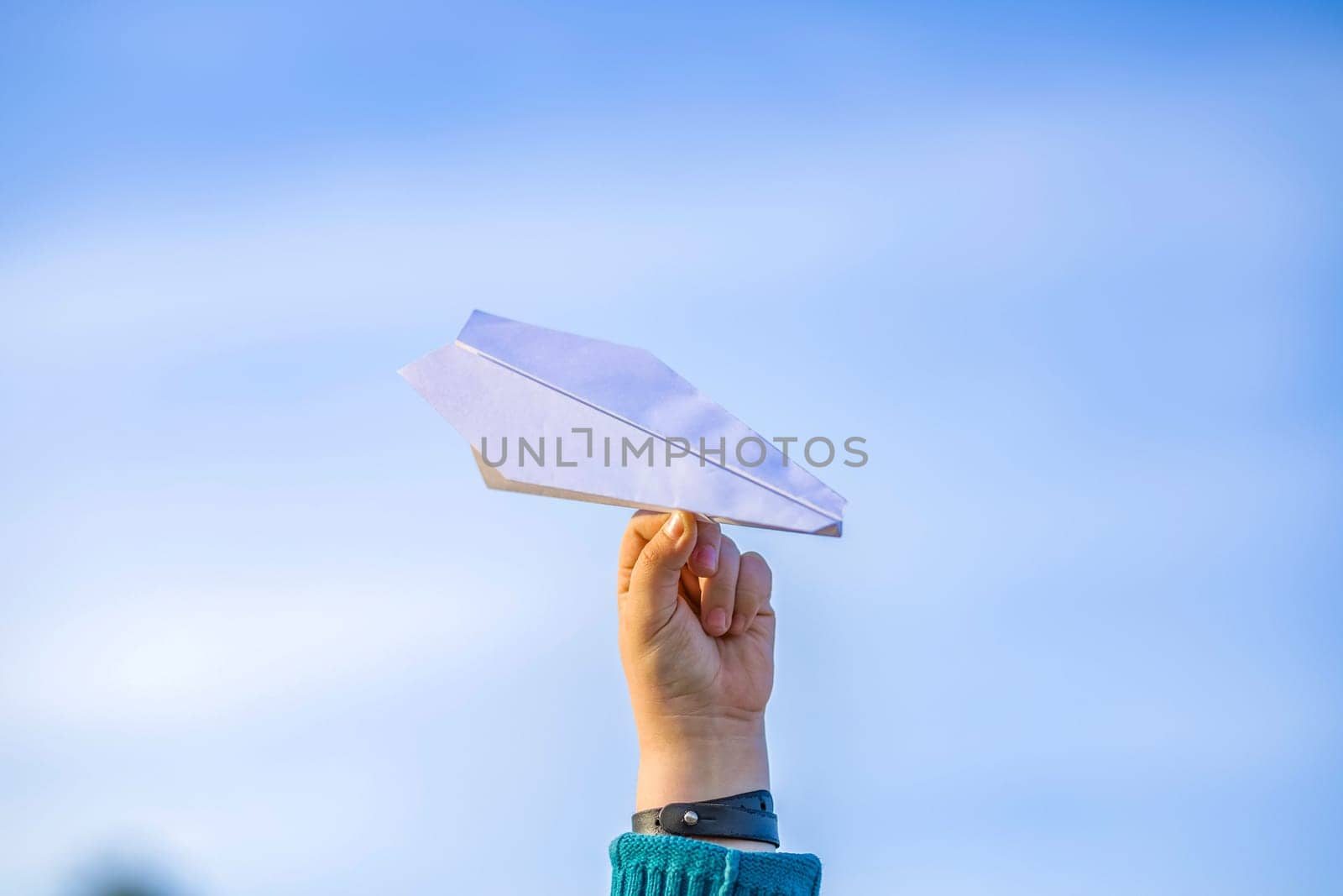 The boy's hand holds a white paper airplane against the sky. The topic of travel and air travel
