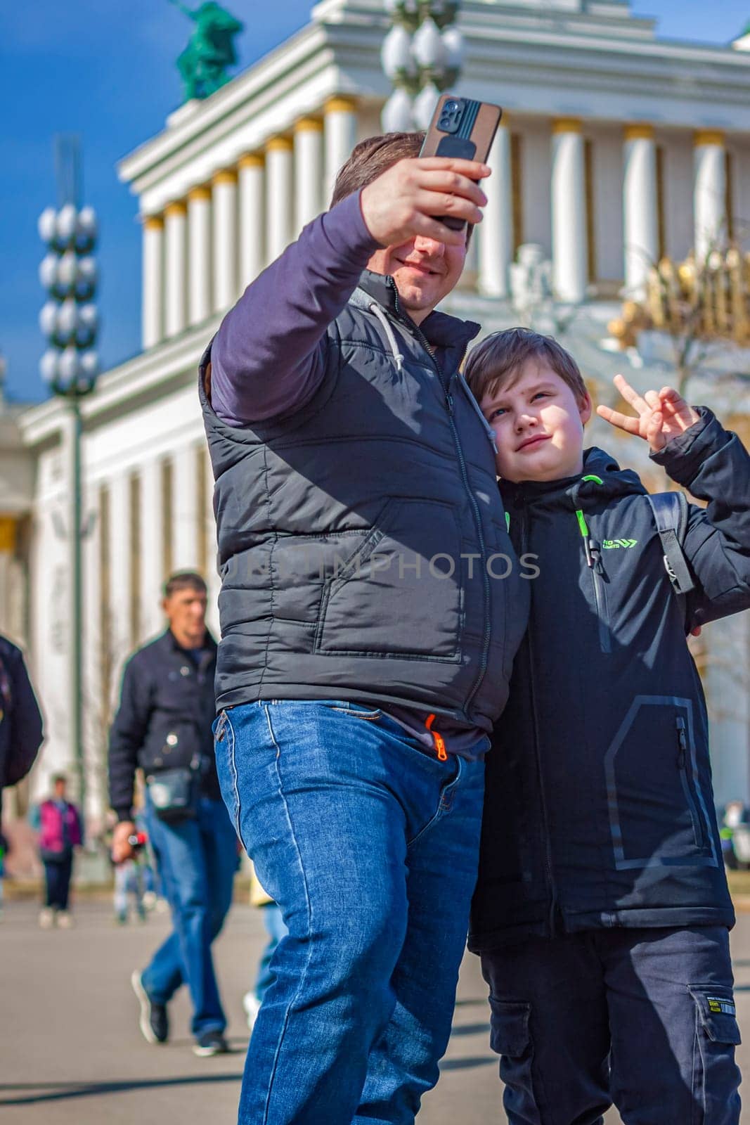 2023-04-08. Moscow, Russia. A man and a boy take a selfie on a smartphone in the city center near an architectural building.  by Alina_Lebed