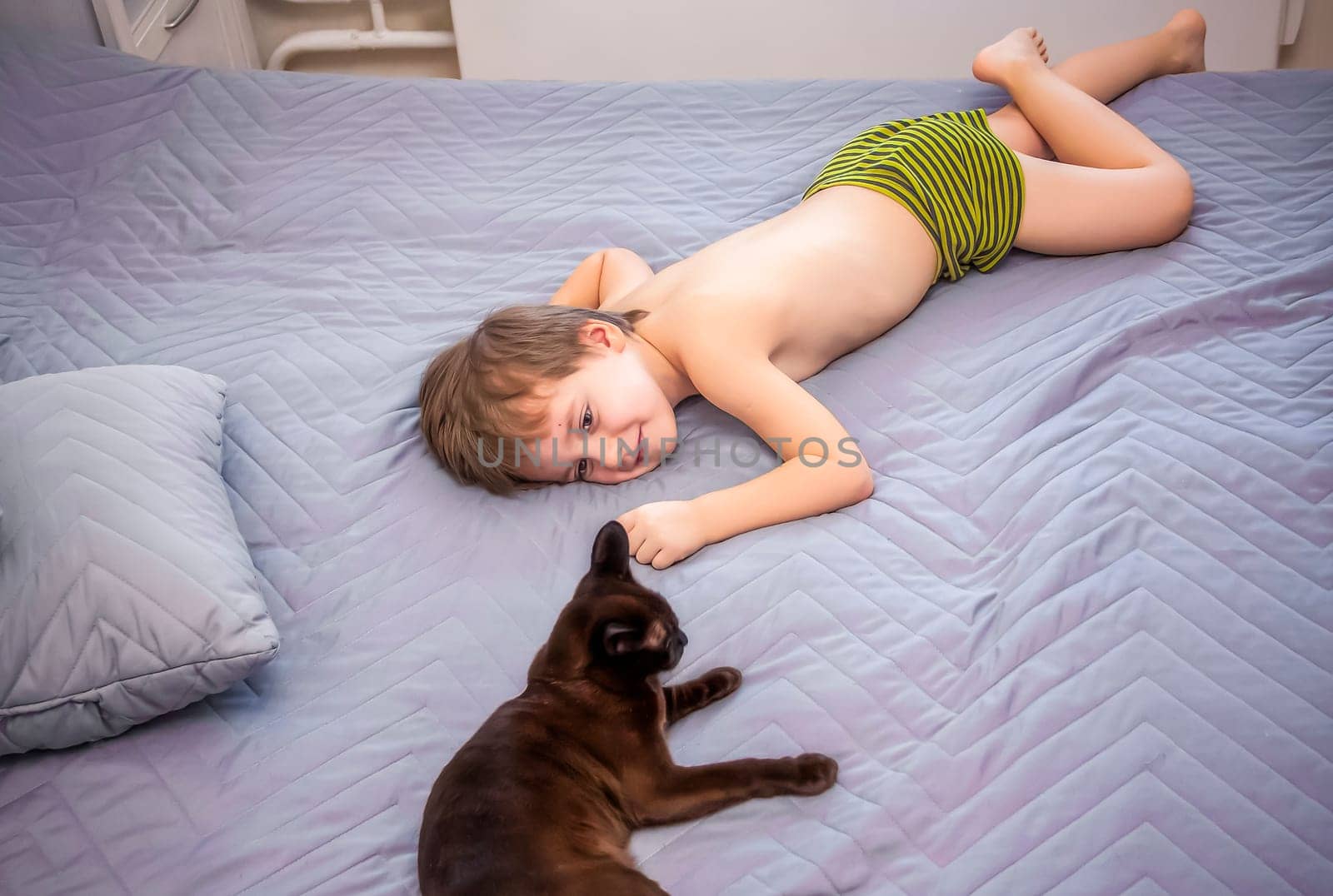 Cute boy without a T-shirt. A blond-haired boy is lying on the bed in a natural setting, and a cat is next to him. The face expresses natural emotions. Not staged photos from nature.