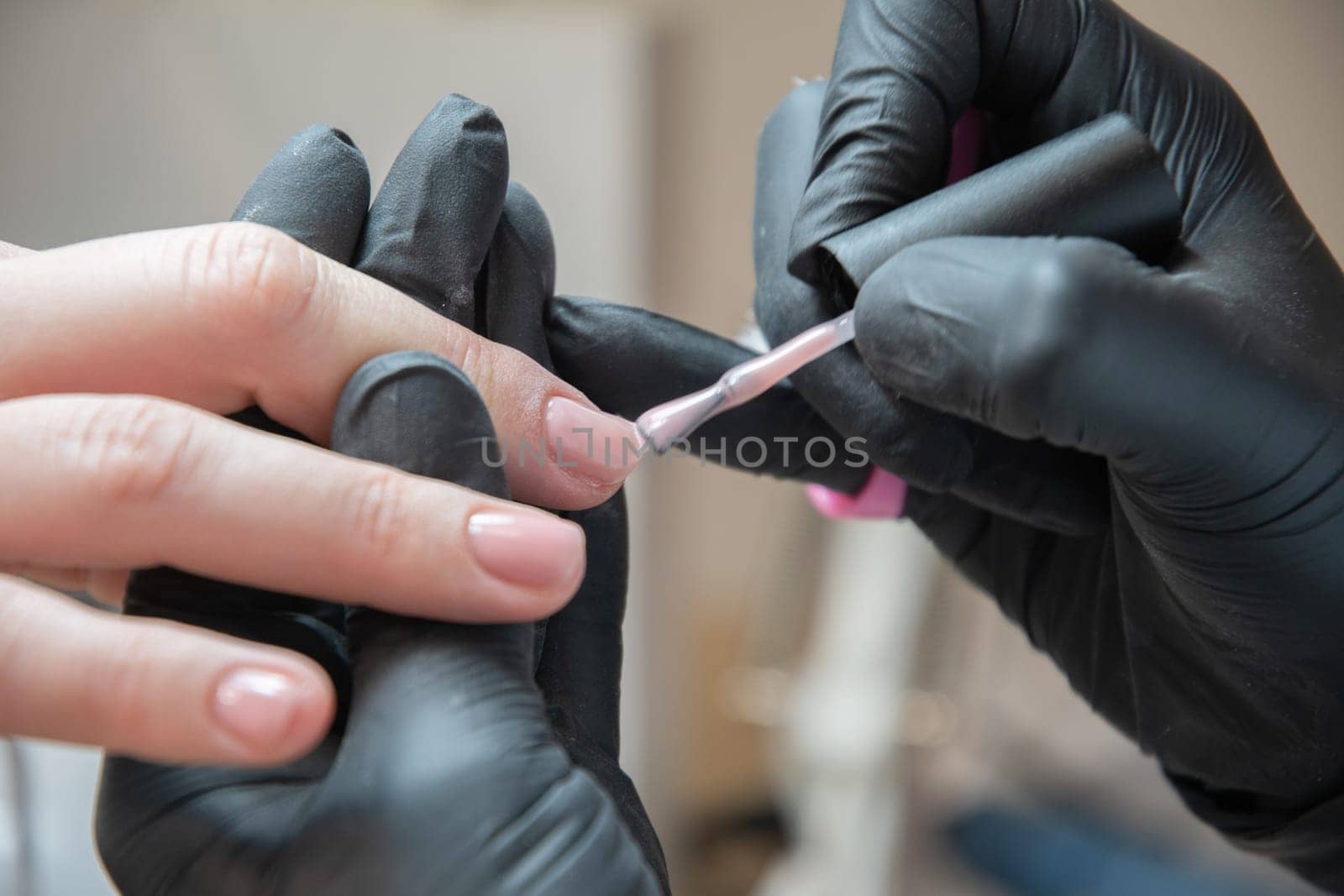 a master does a manicure to a client in a beauty salon and covers her nails with pink varnish. High quality photo