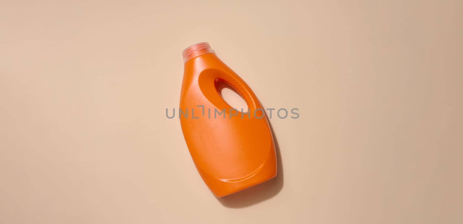 Orange plastic bottle for liquid detergents, for washing clothes on a beige background, top view by ndanko
